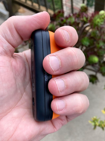 A person holding a small electronic device with an orange and black design