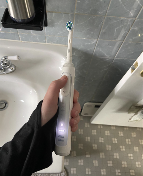 A reviewer holding a white toothbrush, with the settings lit up on the handle, showcasing the features.