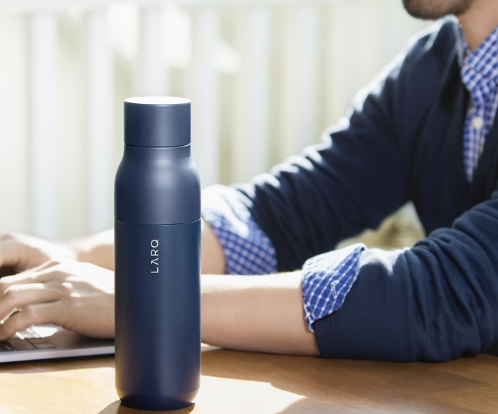 A person sitting at a desk with a LARQ water bottle; the text highlights that it keeps water cold for 24 hours and hot for 12 hours