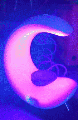 A moon lamp transitioning between different colors on a bedside table.