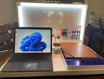 A white briefcase opened to reveal compartments for a laptop, chargers, a dry erase board, and additional storage.