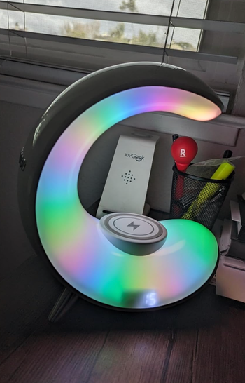 A circular LED desk lamp with a wireless charging pad, surrounded by stationery and a box.