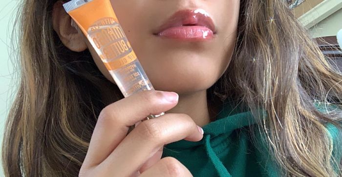A reviewer showcasing glossy lips while holding up the lip gloss.