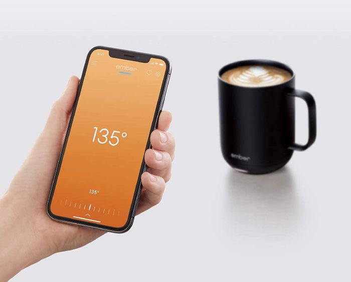 A model holding a smartphone in front of the Ember mug, showing the accompanying app in action.