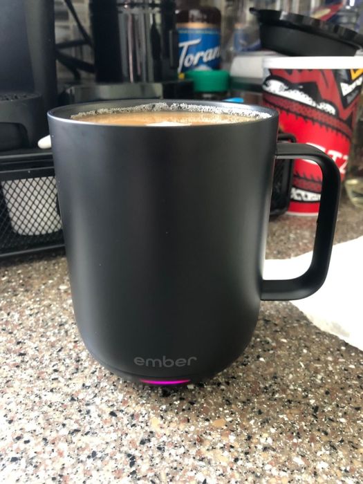 A reviewer’s photo of a black Ember mug filled with steaming coffee.