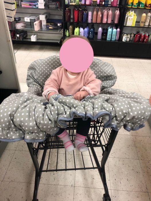 a child in a shopping cart with a gray cover featuring white polka dots