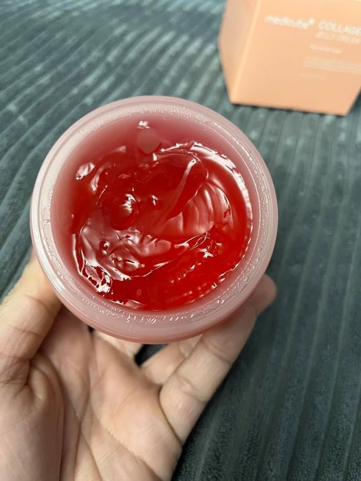A person holding an open jar of Medicube Collagen Gel, displaying the gel's texture with the box packaging visible in the background