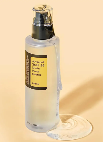 A clear bottle of COSRX Advanced Snail 96 Mucin Power Essence with a black pump, showcasing the product spilling slightly at the base