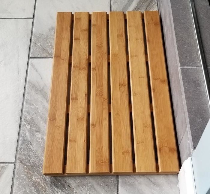 a reviewer's snapshot of the bamboo slatted mat placed elegantly on their bathroom floor