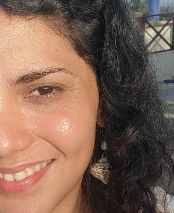 A smiling reviewer with wavy hair, showcasing one side of her face while wearing a dangling earring