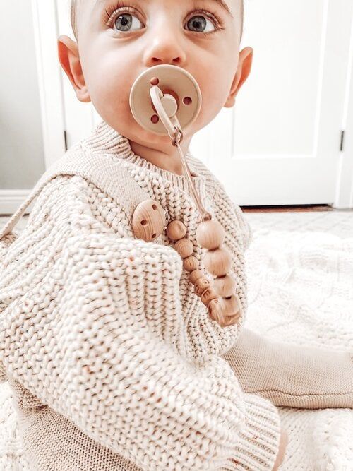 A child with a pacifier in their mouth, attached to a pacifier clip