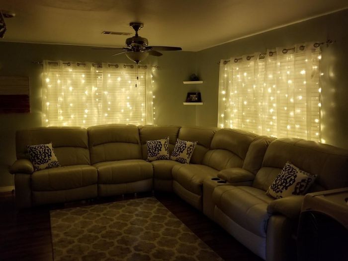 a reviewer's photo of the string lights draped behind sheer curtains, creating a magical glow in a dimly lit living room