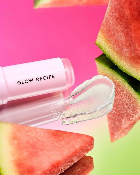 Glow Recipe Watermelon Glow Lip Pop product showcased alongside watermelon slices on a reflective surface, with a vibrant background