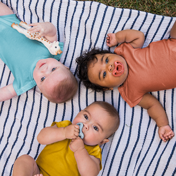 Three babies wearing onesies in blue, orange, and yellow.