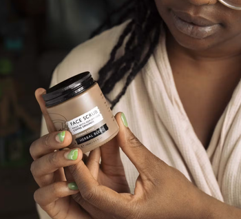 A model holding the tin of the exfoliating face scrub.