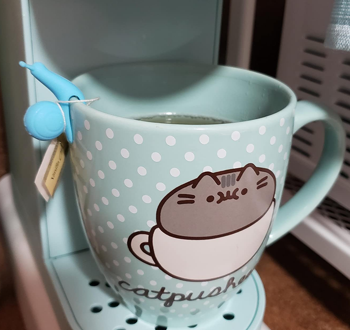A reviewer’s photo showing a blue snail-shaped tea bag holder perched on the edge of a mug