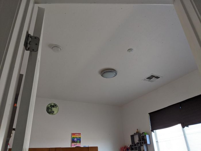 A minimalist bedroom ceiling featuring a round light fixture and smoke detector, visible through an open door