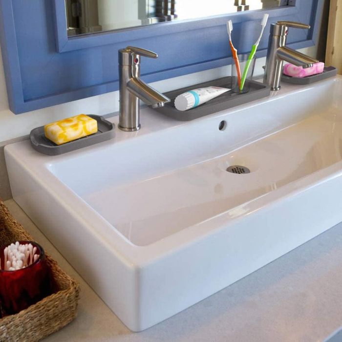 Gray silicone trays placed on a bathroom sink, neatly holding soap and other personal care items