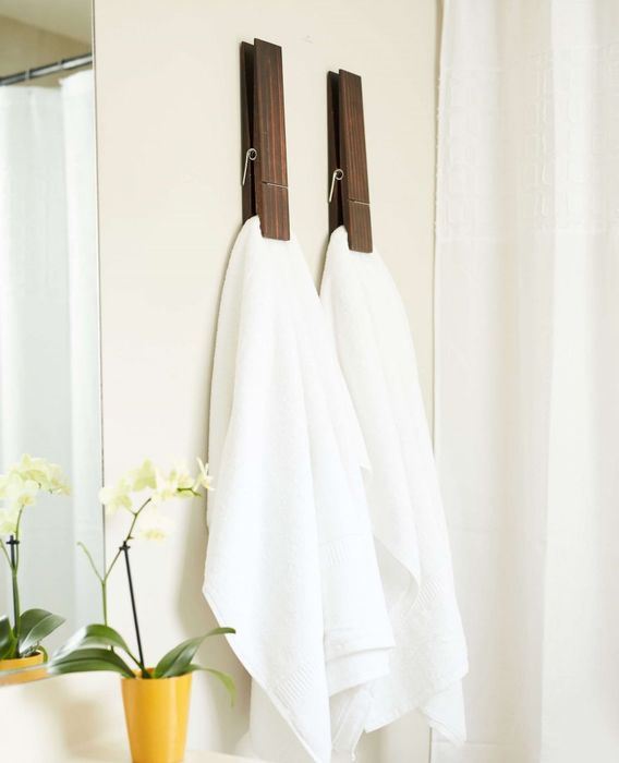 Two oversized clothespin hooks mounted on a wall, neatly holding towels in place