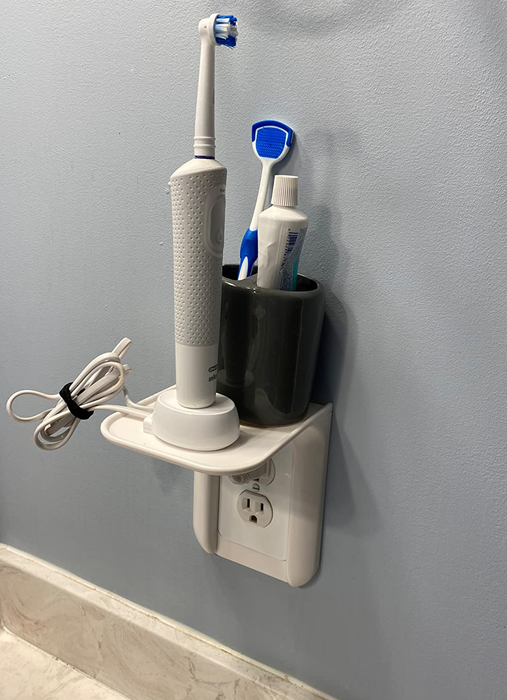 Photo from a reviewer showing a white outlet shelf holding an electric toothbrush and a toothpaste holder