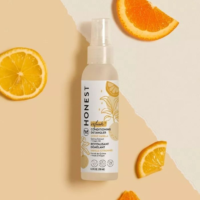 A bottle of Honest Beauty Conditioning Detangler surrounded by fresh citrus slices, with the images of orange and lemon slices on the label