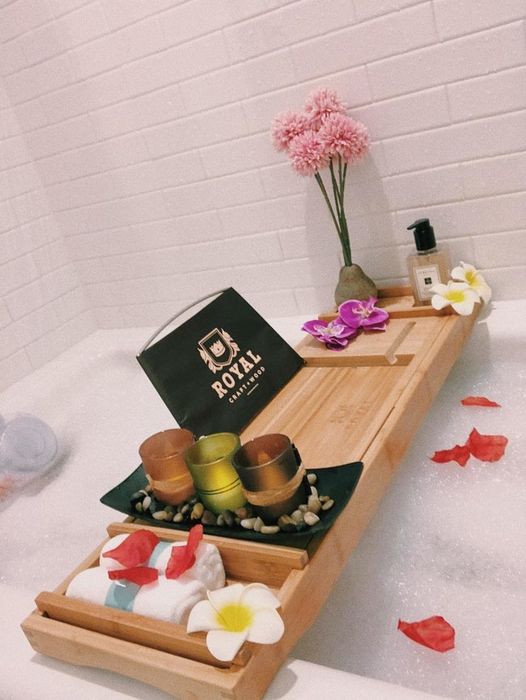 Reviewer photo of a natural-colored bathtub tray adorned with candles and flowers, set over a bubble bath