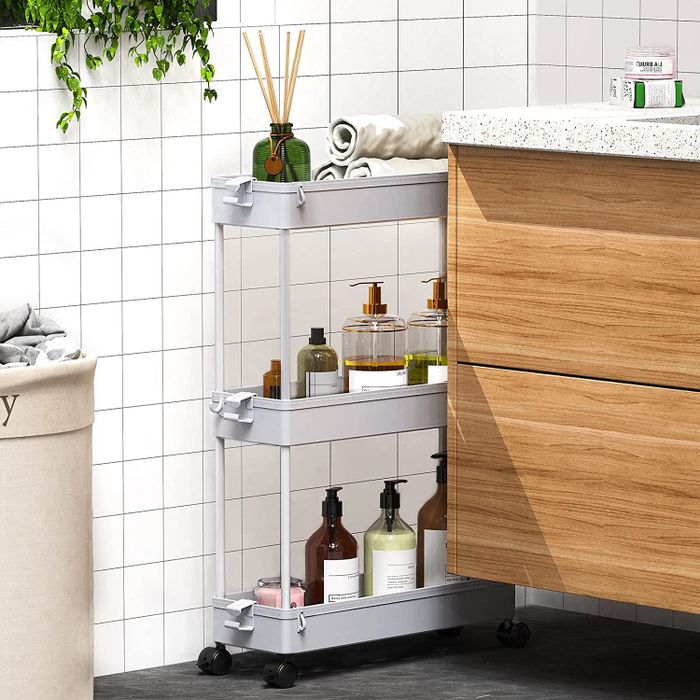 A three-tiered storage cart positioned snugly between a wall and a bathroom counter