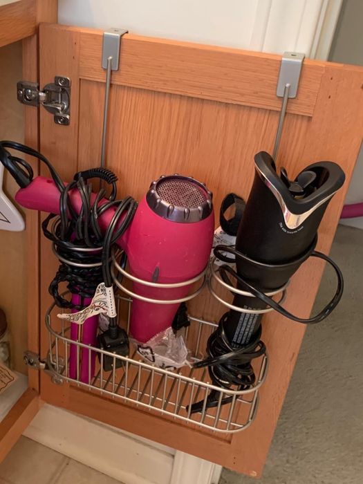 A reviewer’s over-the-door organizer is displayed hanging on a bathroom cabinet door, efficiently holding various styling tools.