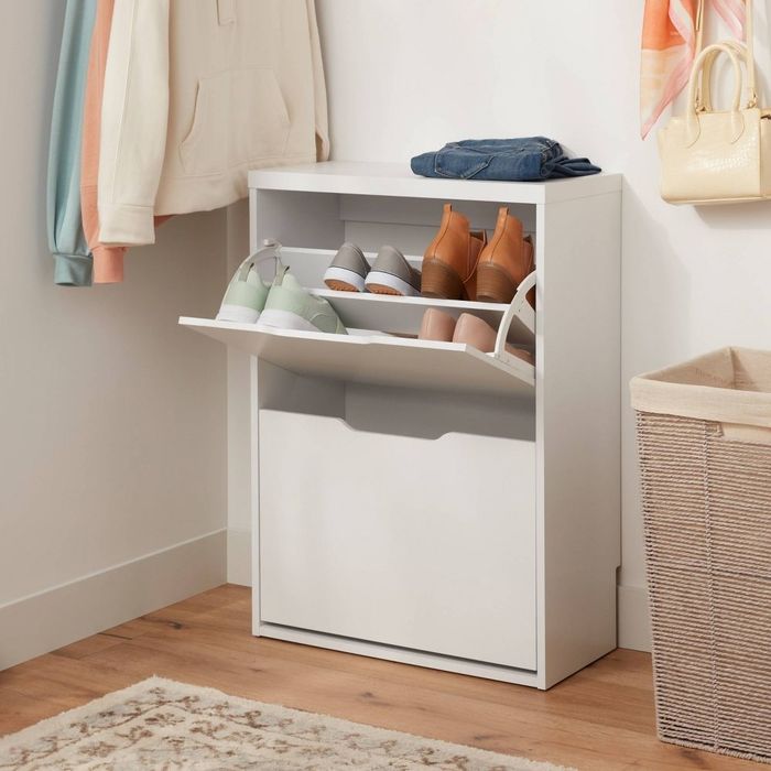 A shoe cabinet in a closet holds a variety of footwear. A pair of jeans and a purse rest on top, making it an ideal space-saving organizer.