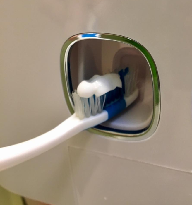 Another reviewer demonstrates the toothpaste dispenser in action, showing a toothbrush being pressed against it to release toothpaste.