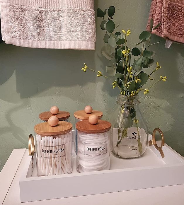 A reviewer’s photo shows labeled glass jars with bamboo lids, filled with Q-tips and cotton pads, arranged on a tray alongside a vase of eucalyptus.