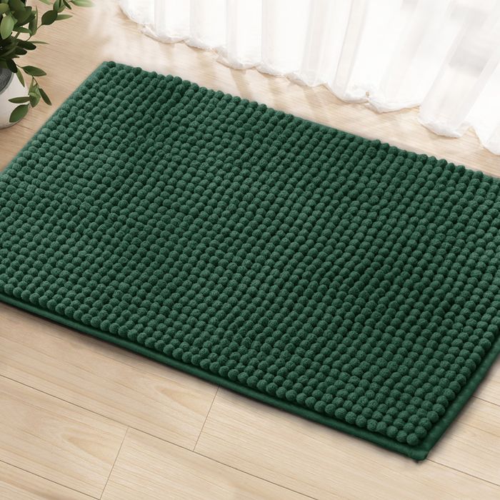 A green textured doormat placed on a wooden floor next to a sheer curtain