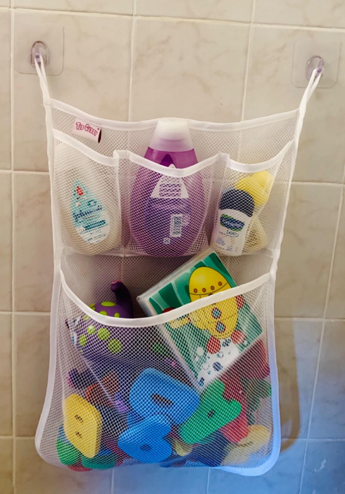 Reviewer's photo of a bath organizer with mesh pockets filled with toys and other items, securely attached to the shower wall using suction cups