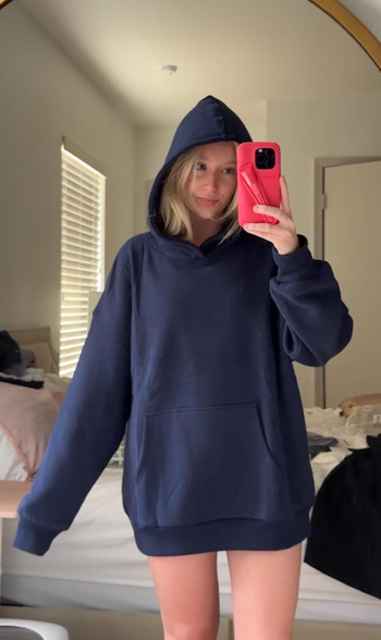 A reviewer wearing a navy blue oversized hoodie and taking a mirror selfie.