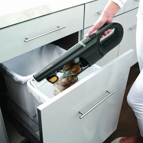 A handheld vacuum is emptied into a trash can