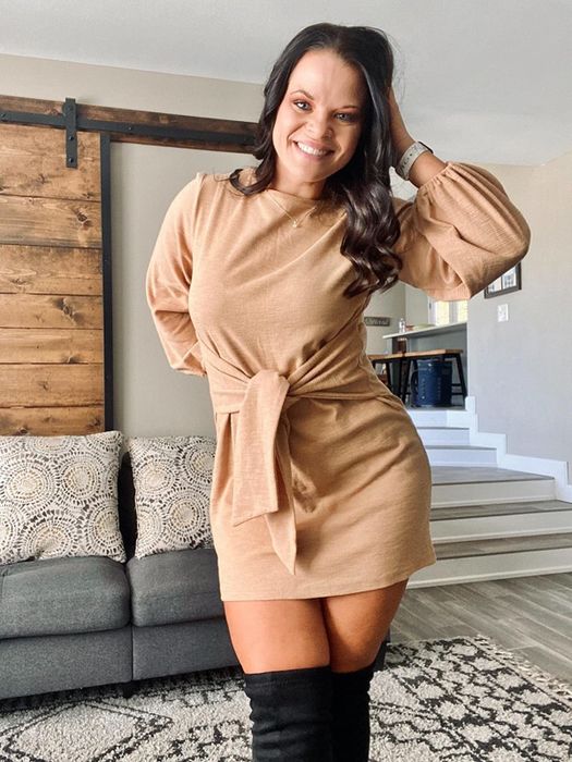 A reviewer wearing a sand-colored long-sleeve dress that stops mid-thigh.