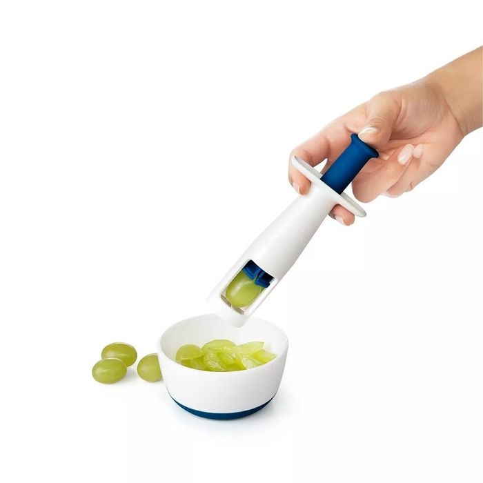 A hand demonstrates the use of a grape cutter