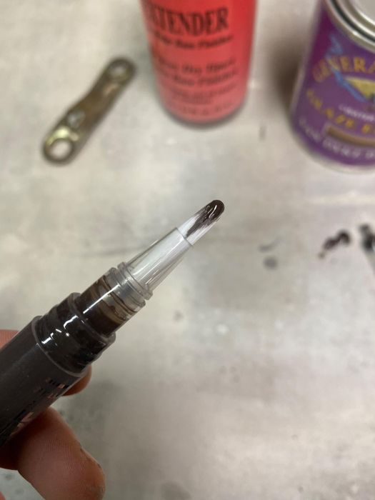 person holding a pen with a leaking ink cartridge, with blurred tools and containers in the background