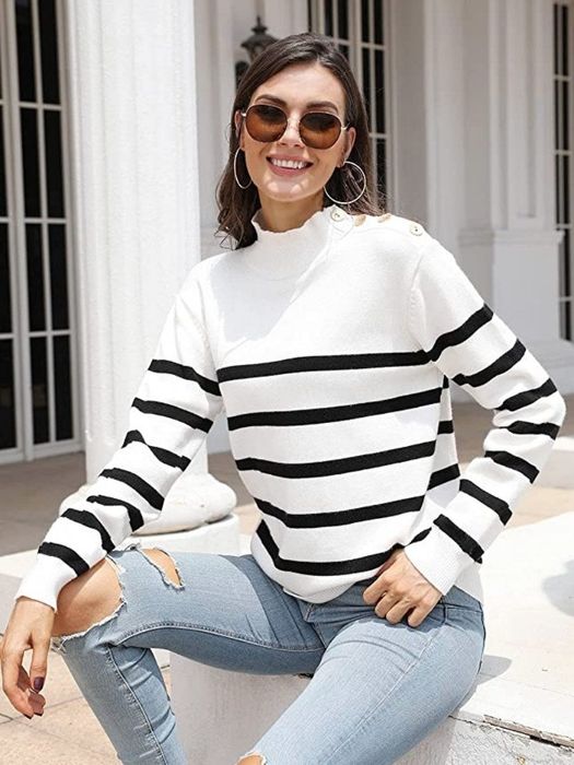 A model showcases a white and black striped pullover turtleneck sweater adorned with decorative shoulder buttons.