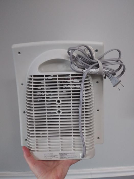 A reviewer holding their space heater, showing the cord bundler neatly securing the heater’s cord to the back of the machine.