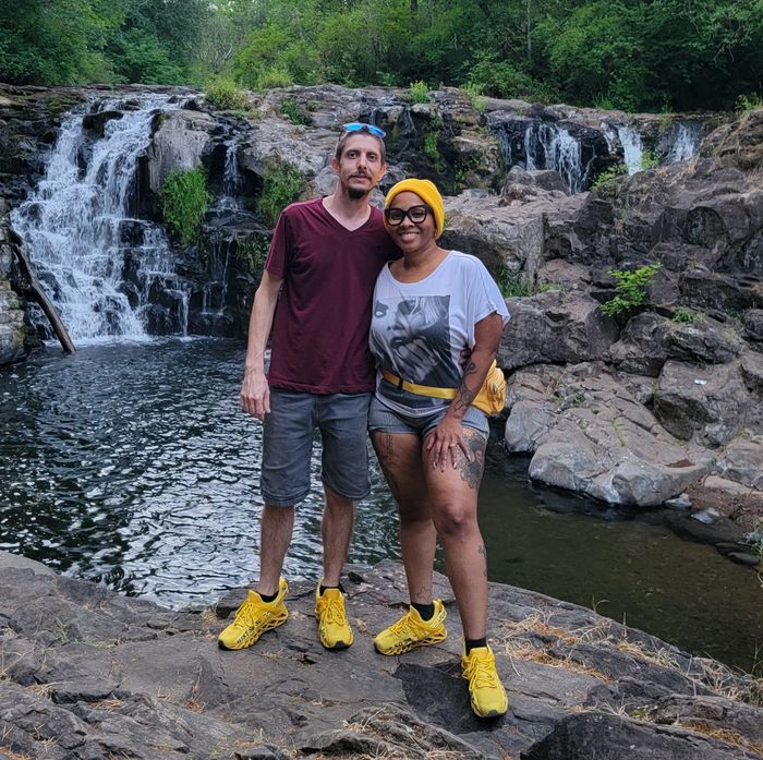 Two reviewers showing off their yellow sneakers in front of a waterfall.