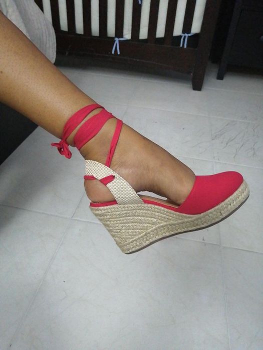 A person wearing a red wedge espadrille shoe with ankle ties