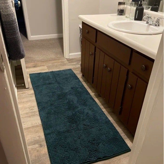 A reviewer photo of a large bath mat placed beneath a double sink, providing comfort and preventing water from spreading.