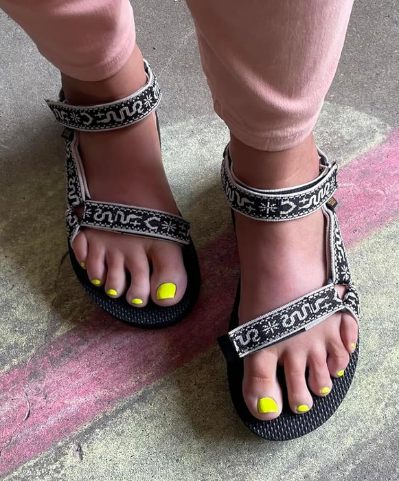 A person wearing black sandals with unique strap designs