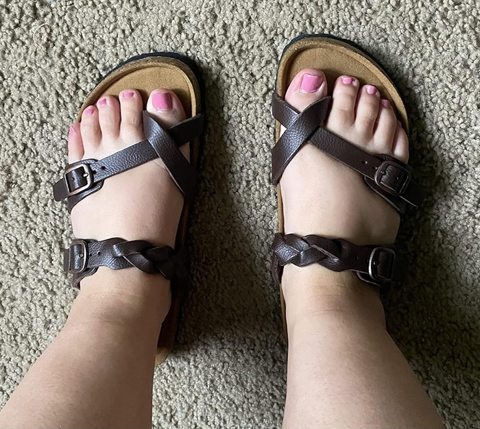Person wearing dark strappy sandals with buckles, viewed from above