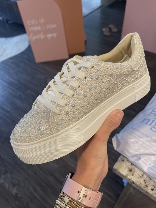 A hand holding a glittery sneaker adorned with rhinestones and pearls
