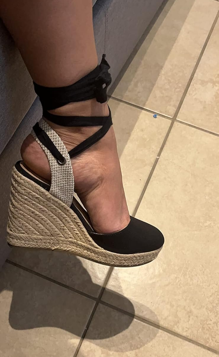 A person trying on a black-tie ankle strap wedge shoe