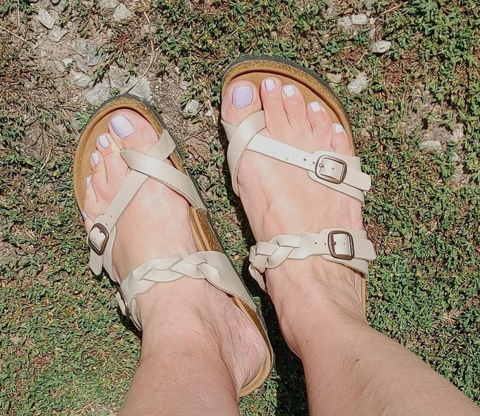 A pair of feet wearing strappy sandals with buckles, shown from above