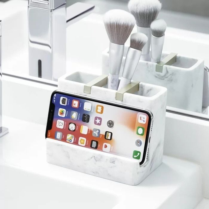 A bathroom organizer with three sections, featuring a phone holder, placed on a sink ledge for easy access.