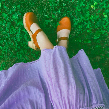 A reviewer's feet adorned in clogs, set against a clover-filled backdrop while wearing a dress